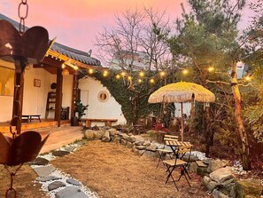 Un bâtiment de style japonais traditionnel, doté d’un parasol en chaume, d’un chemin de pierre et d’un espace de repos extérieur.