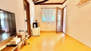 A room with a wooden ceiling, a flat-screen TV, a small table with a tissue box, a basket, and a white appliance.