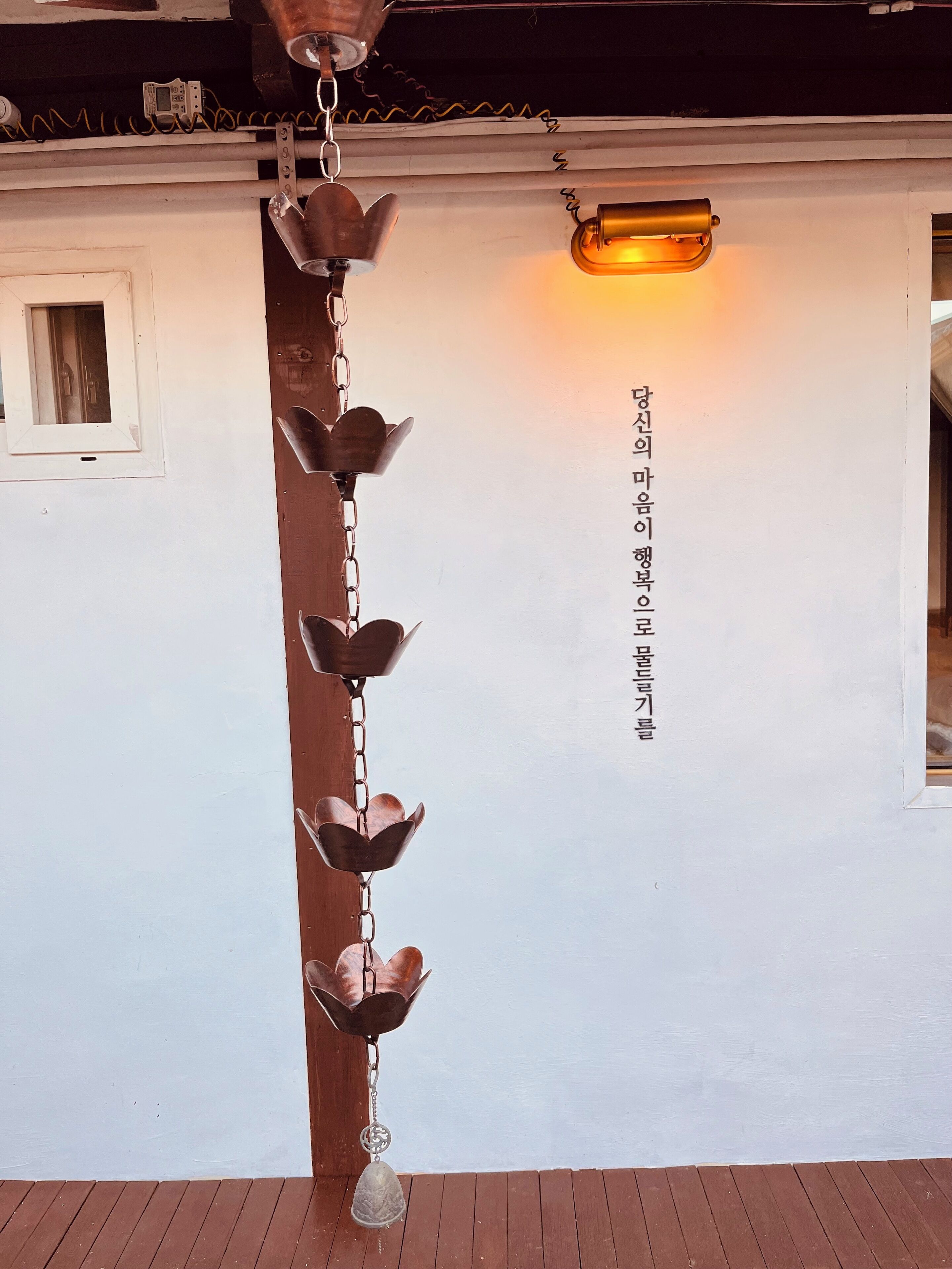 A metal wind chime hanging from a ceiling, a small window, and a wall-mounted light fixture.
