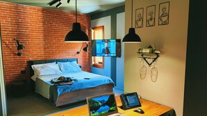 Un dormitorio moderno con pared de ladrillo, una cama, un escritorio con una computadora portátil y un televisor.