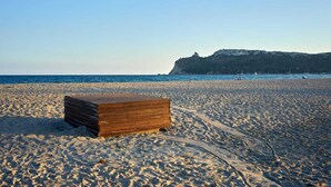 Un cofre de madera sobre una playa arenosa, con un cielo despejado y un acantilado rocoso a lo lejos.