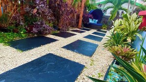 A garden pathway with black and white tiles, surrounded by various plants and a wooden fence.