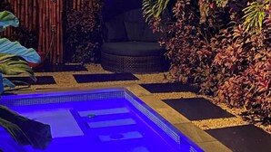 A pool area with a tiled deck, surrounded by plants and a bamboo fence.
