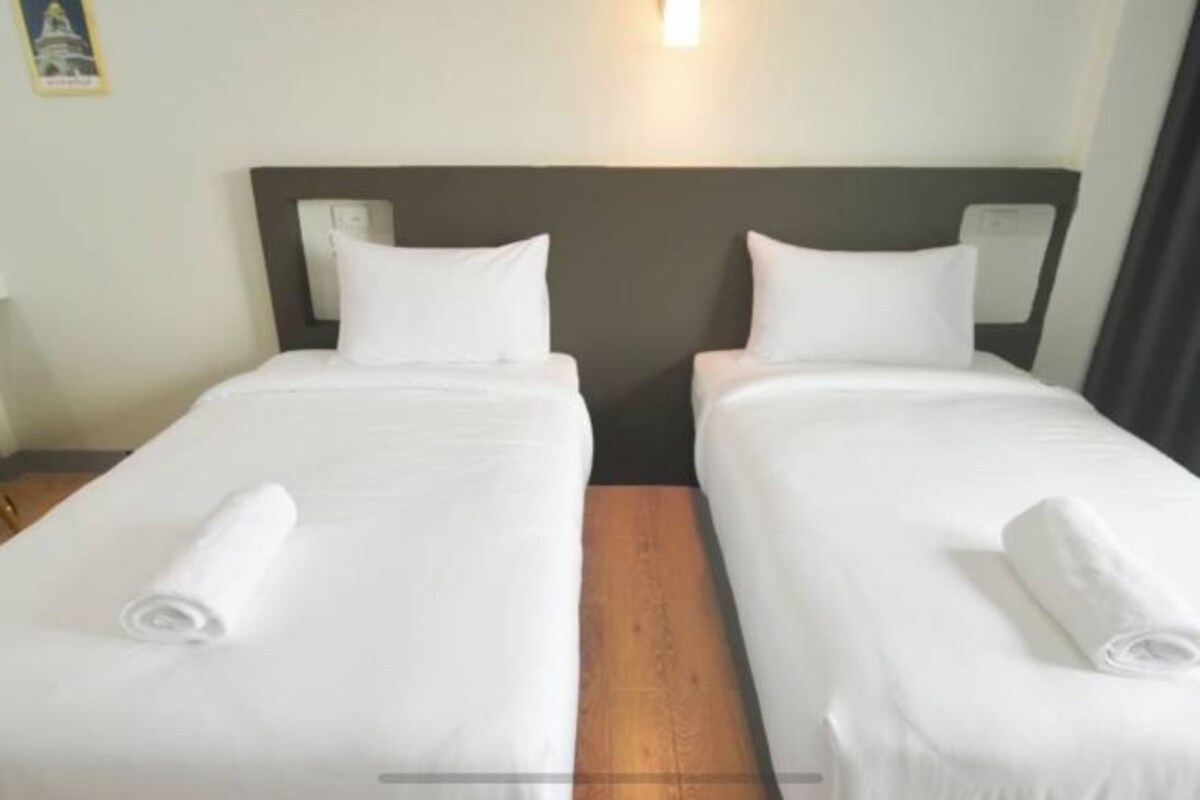 Habitación de hotel con dos camas individuales, cada una con colchón y almohada blancos, y cabeceros de madera.