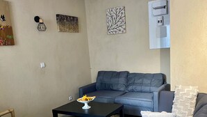 A living room with a sofa, a coffee table, and two chairs. There are wall decorations and an air conditioning unit. - MAISON RURAL A ST CLEMENT DE VALORGUE  (Saint-Clément-de-Valorgue)