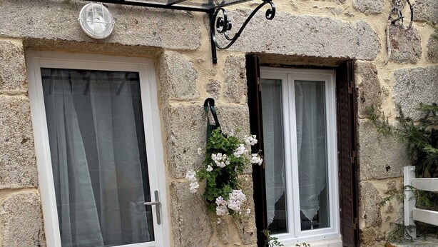 A stone building with a white door and window, a small garden with flowers, and a wooden bench. - MAISON RURAL A ST CLEMENT DE VALORGUE  (Saint-Clément-de-Valorgue)