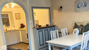 A dining area with a white table and chairs, a wooden bench, and a kitchen in the background. - MAISON RURAL A ST CLEMENT DE VALORGUE  (Saint-Clément-de-Valorgue)