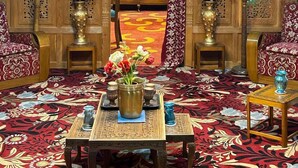 A room with a chandelier, ornate wooden paneling, a patterned carpet, and a table with a vase of flowers. - The Mughal Palace Eco Luxury Houseboat  (Srinagar)