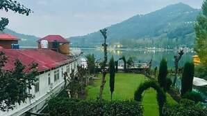A view of a building with a red roof, a grassy area, and a lake in the background. - The Mughal Palace Eco Luxury Houseboat  (Srinagar)
