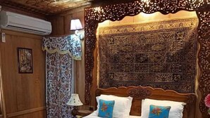 A wooden-paneled room with a large bed, patterned curtains, and a decorative headboard. - The Mughal Palace Eco Luxury Houseboat  (Srinagar)