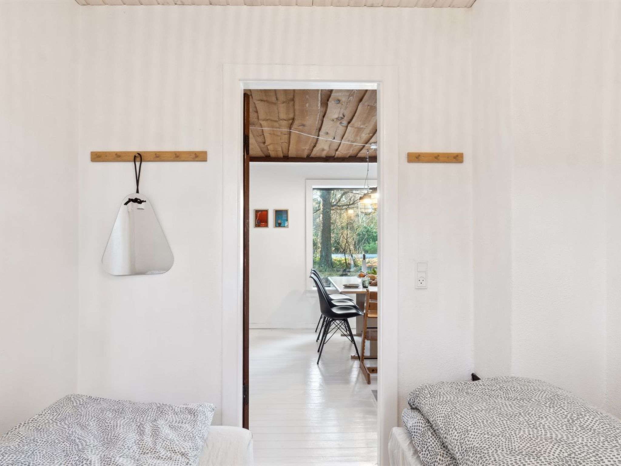 A minimalist room with a wooden ceiling, a white pendant light, and a view of an outdoor dining area through a doorway.