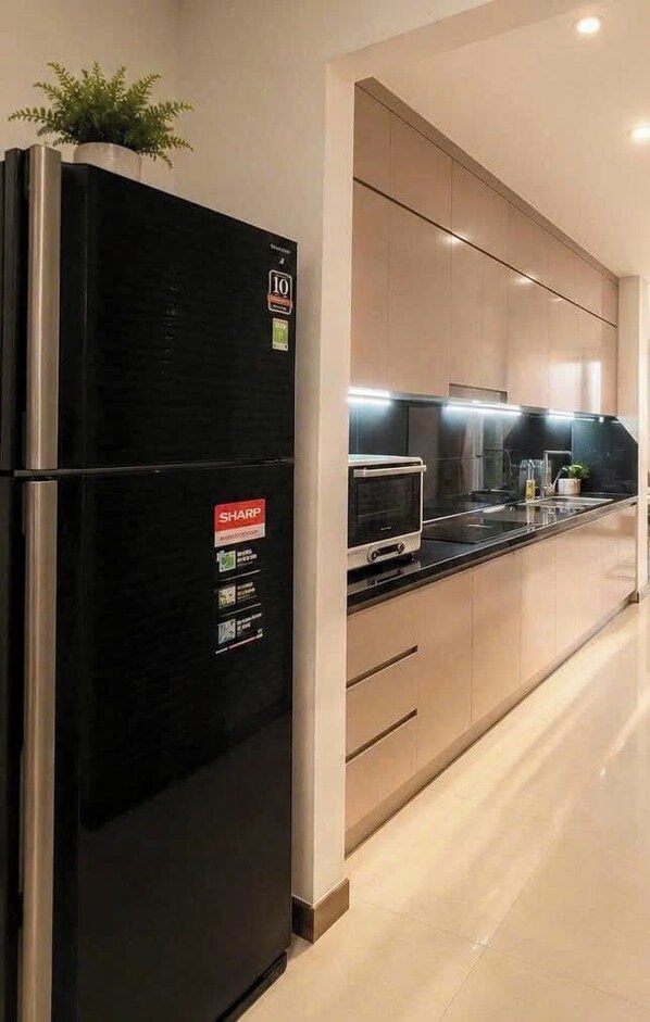 A modern kitchen with a black refrigerator, a microwave, and a sink. - Ha Do Centrosa - Luxury Central Point (Ho Chi Minh City)