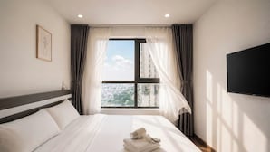 Habitación de hotel con cama, televisión, ventana con cortinas y vista a la ciudad.