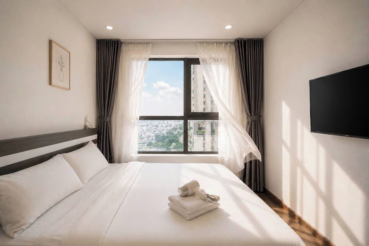 Habitación de hotel con cama, televisión, ventana con cortinas y vista a la ciudad.