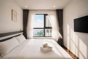Habitación de hotel con cama, televisión, ventana con cortinas y vista a la ciudad.