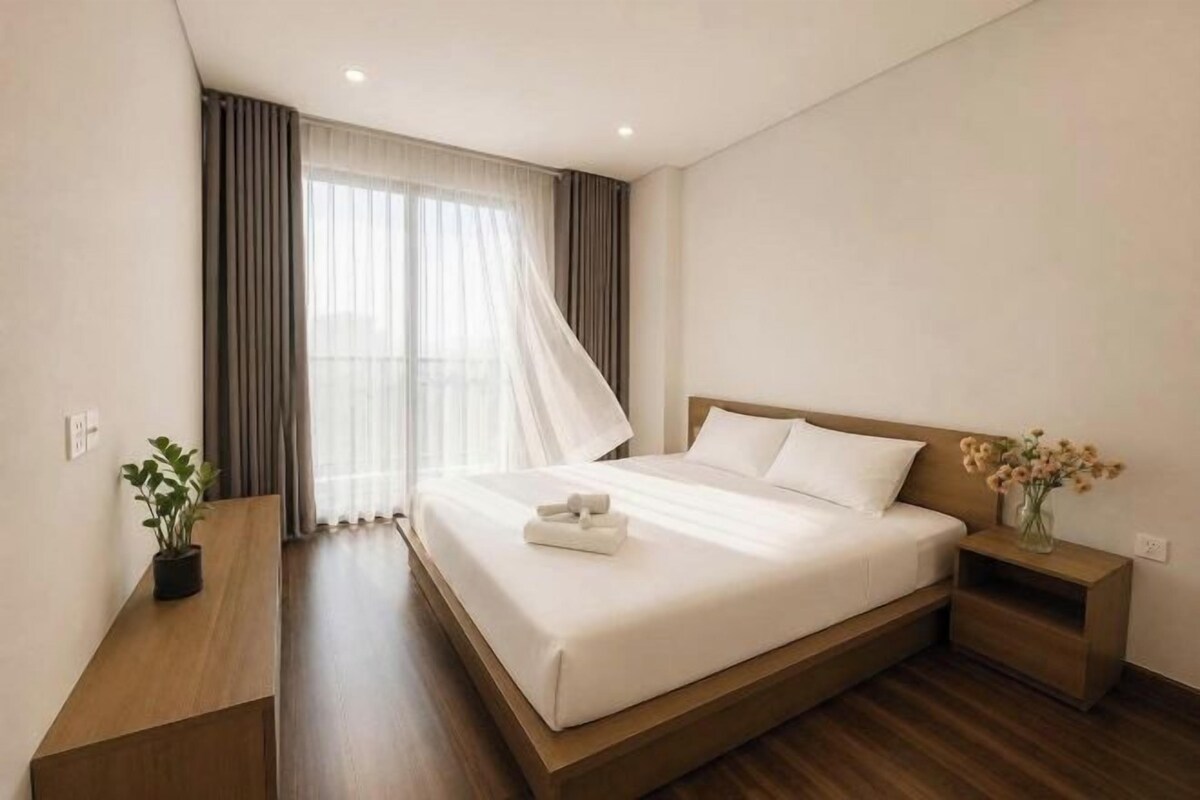 Ein Hotelzimmer mit einem großen Bett, einem Nachttisch, einem Fenster mit Vorhängen und einer kleinen Pflanze.
