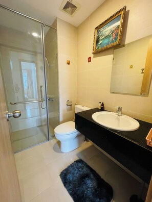 A bathroom with a glass shower enclosure, a white toilet, a black sink, and a mirror above the sink. - Charmington La Pointe - Central Suites D (Ho Chi Minh City)