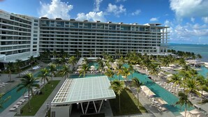 Een groot hotel met meerdere verdiepingen, een zwembadgedeelte met palmbomen en uitzicht op de oceaan.