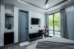 Een moderne slaapkamer met een bed, een bureau, een televisie en een balkon met gordijnen.