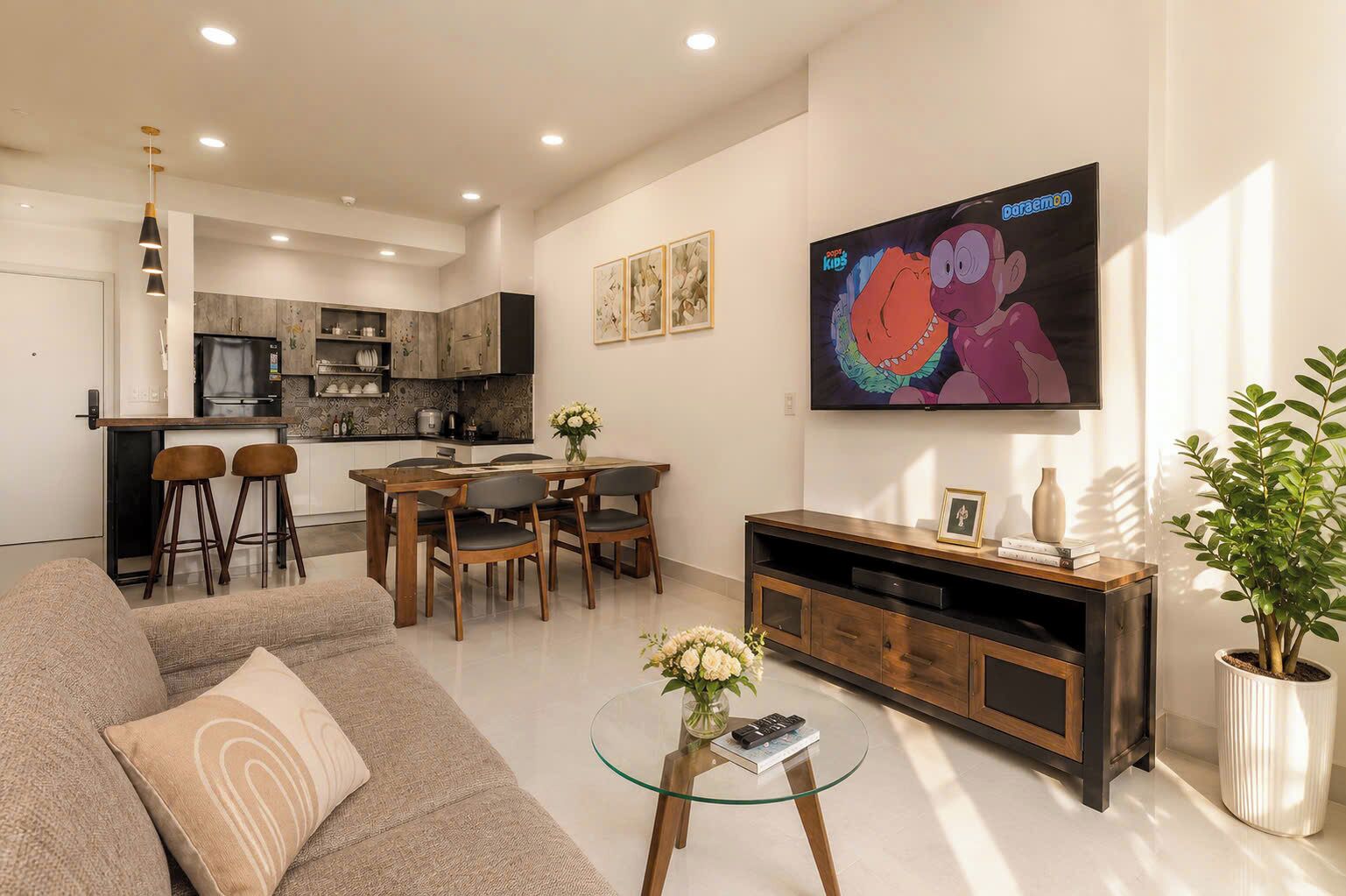 A modern living room with a sofa, dining table, chairs, a TV, and a kitchen in the background.