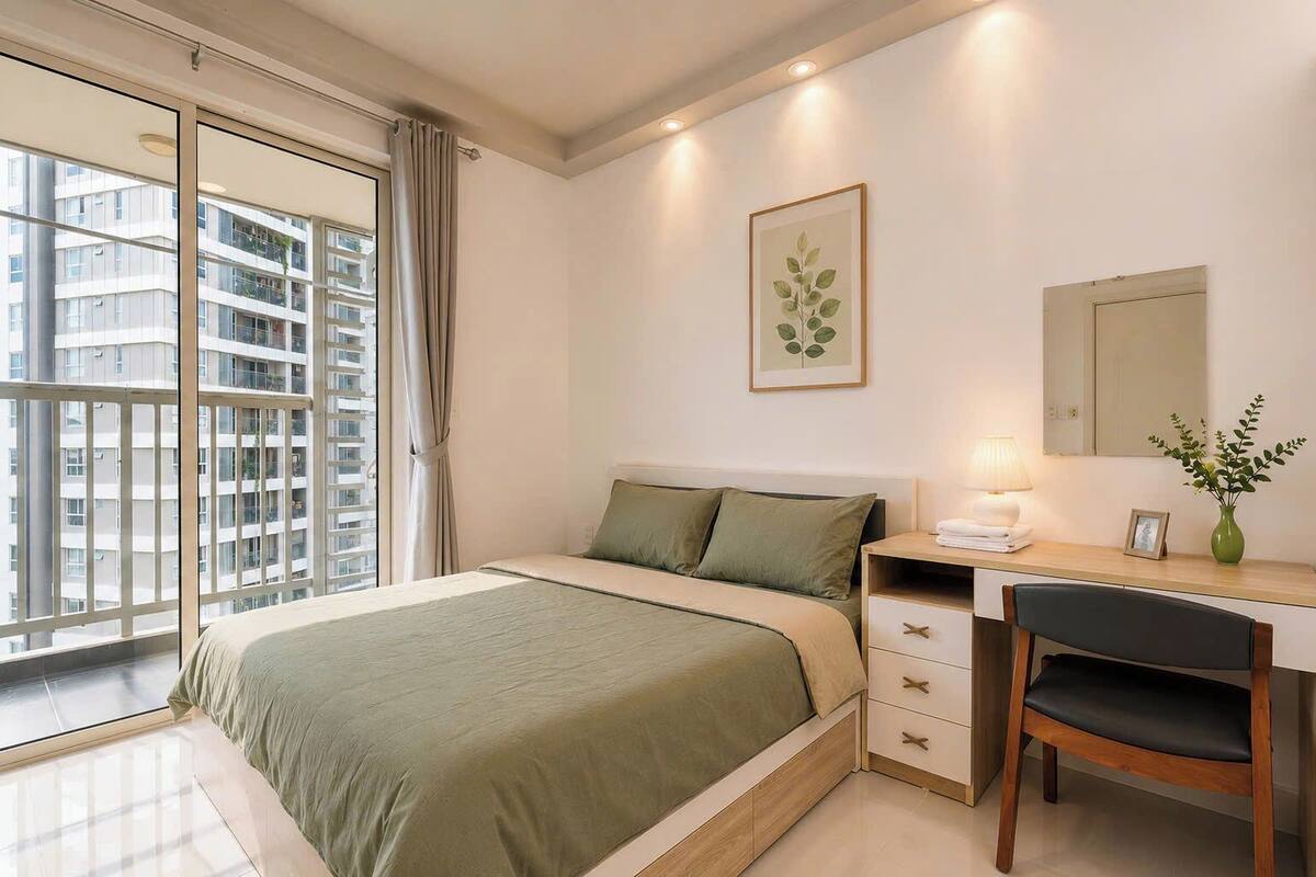 Ein Schlafzimmer mit einem Bett, einem Schreibtisch, einem Sessel, einer Lampe, einer Vase mit Pflanzen, einem gerahmten Bild und einem Fenster mit Vorhängen.