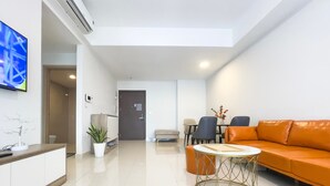 A modern living room with a sofa, a round coffee table, a TV, and a door leading to another room. - Minute Suites - Botanica Orchard TSN Air (Ho Chi Minh City)