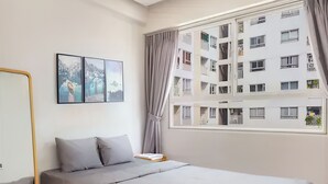A modern bedroom with a bed, a bedside table, a mirror, and a window with a view of a building. - Minute Suites - Botanica Orchard TSN Air (Ho Chi Minh City)