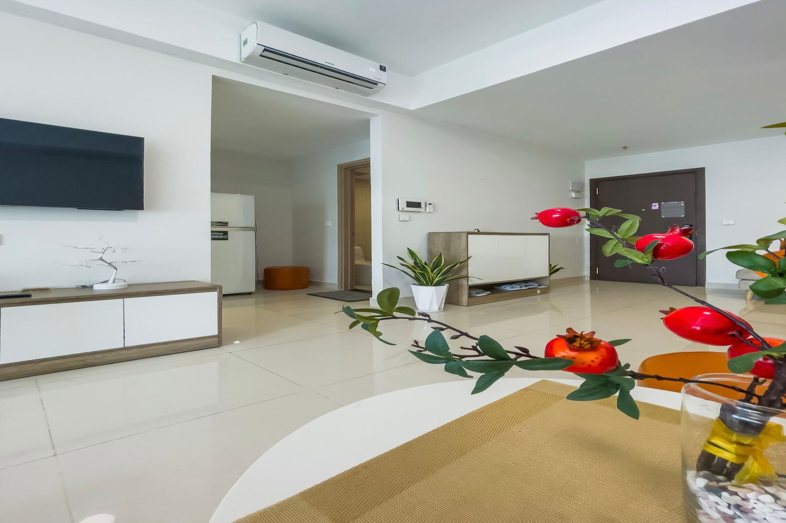 Una sala de estar moderna con un televisor de pantalla plana, una planta en maceta y un jarrón decorativo con flores rojas.