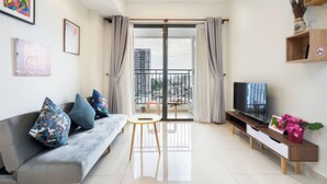 A modern living room with a sofa, TV, and a balcony with curtains. - Minute Suites - Botanica Orchard TSN Air (Ho Chi Minh City)