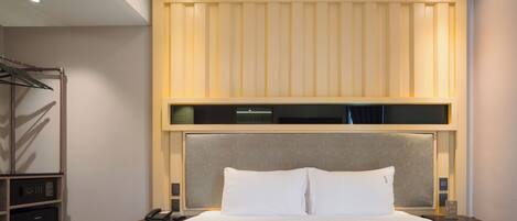 A hotel room with a large bed, a bedside table with a phone, a nightstand, a wardrobe, and a built-in shelf above the bed.