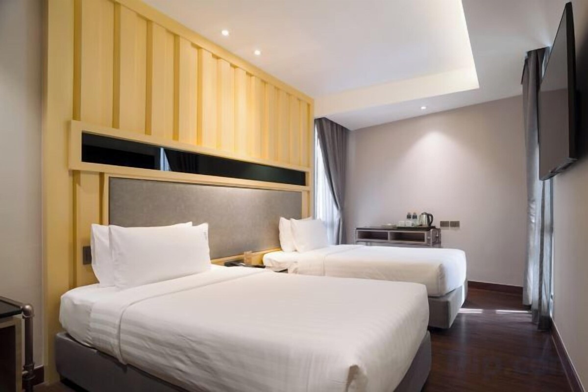 Habitación de hotel con dos camas, cabecero de madera, televisor de pantalla plana y una mesita con hervidor.