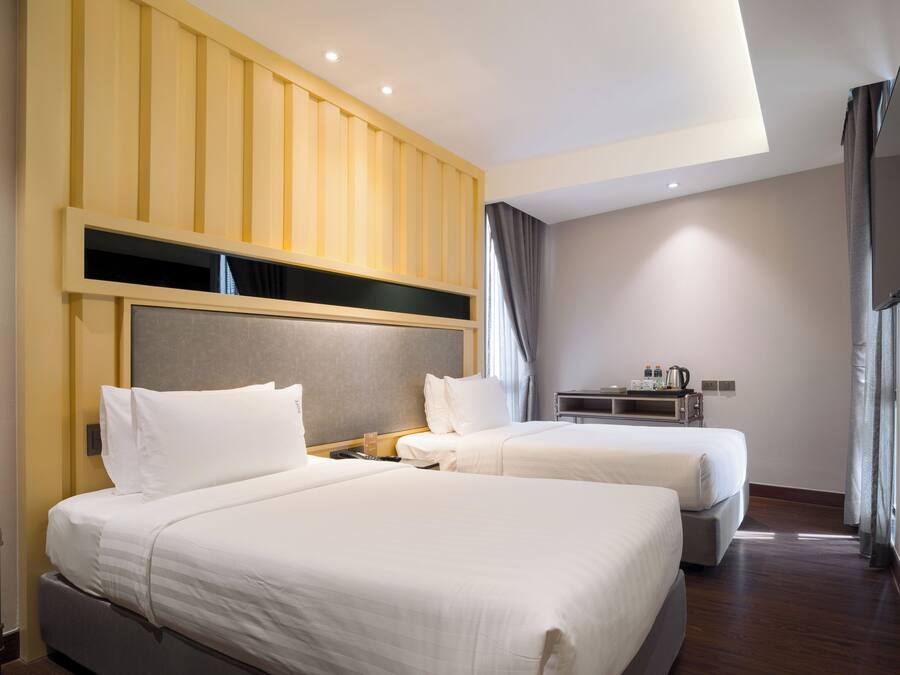 A hotel room with two beds, a wooden panel wall, a flat-screen TV, and a small table with a kettle.