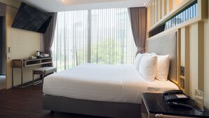 Une chambre d’hôtel moderne dotée d’un grand lit, d’un bureau, d’une télévision à écran plat et d’une fenêtre avec des rideaux.