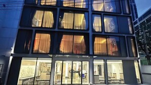 Un bâtiment moderne à plusieurs étages, doté de grandes fenêtres avec des rideaux et d’un hall d’entrée bien éclairé.
