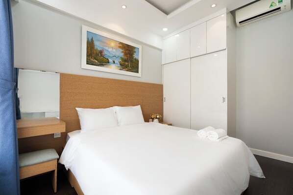 A hotel room with a bed, a wooden headboard, a nightstand with a lamp, a painting on the wall, and a wardrobe. - Golden Mansion - Transit Apt Free POOL & GYM (Ho Chi Minh City)