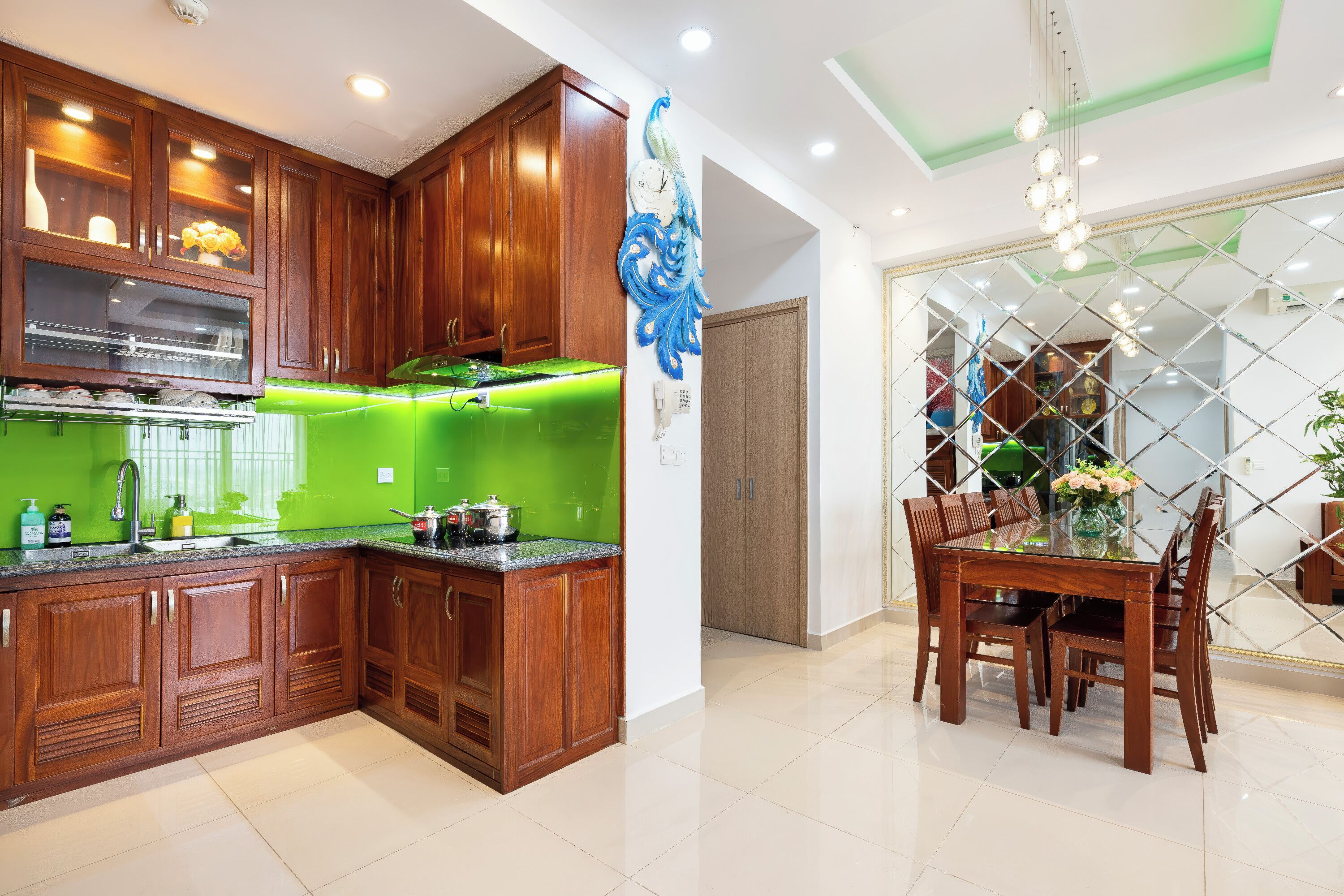 Una cocina moderna con armarios de madera, un salpicadero verde y un comedor con mesa y sillas de vidrio.