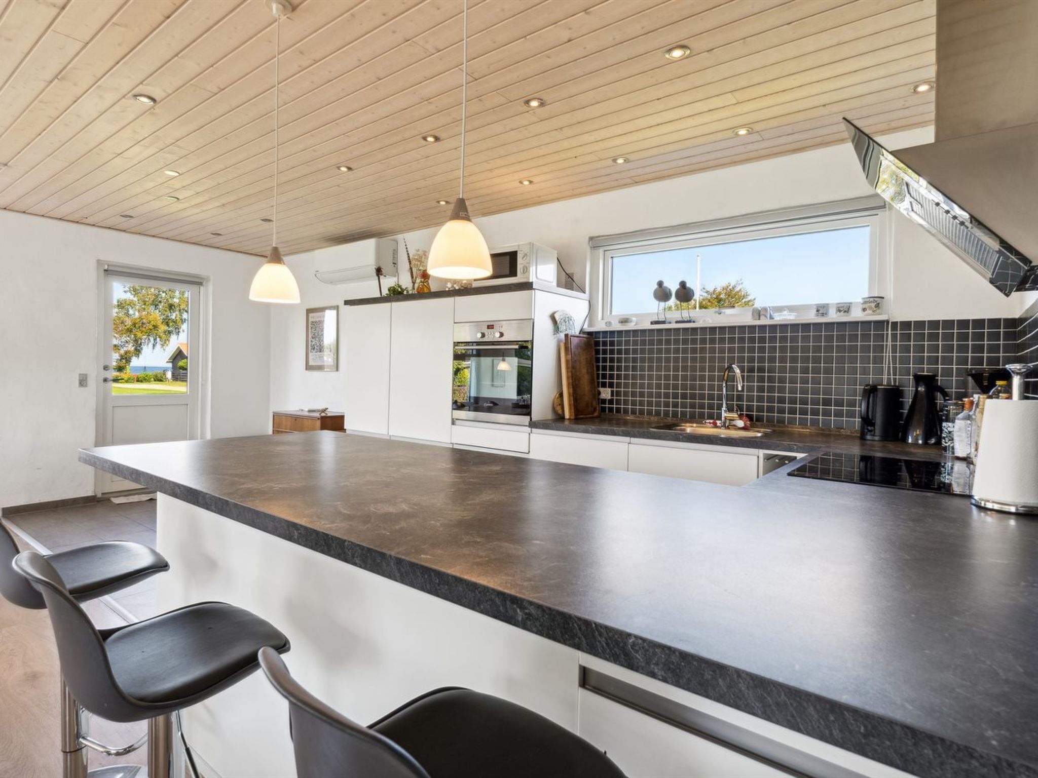 Uma cozinha moderna com uma ilha grande, banquetas, forno embutido e uma janela com vista para o exterior.
