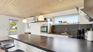 A modern kitchen with a large island, bar stools, a built-in oven, and a window with a view of the outdoors. - "Todor" - 150m from the sea by Interhome (Nordborg)
