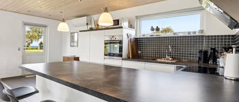 Una cocina moderna con una isla grande, taburetes de bar, horno empotrado y ventana con vistas al exterior.