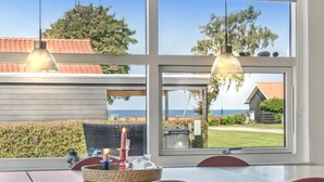 A dining area with a table and chairs, a view of the sea through large windows, and a pergola with hanging lights. - "Todor" - 150m from the sea by Interhome (Nordborg)