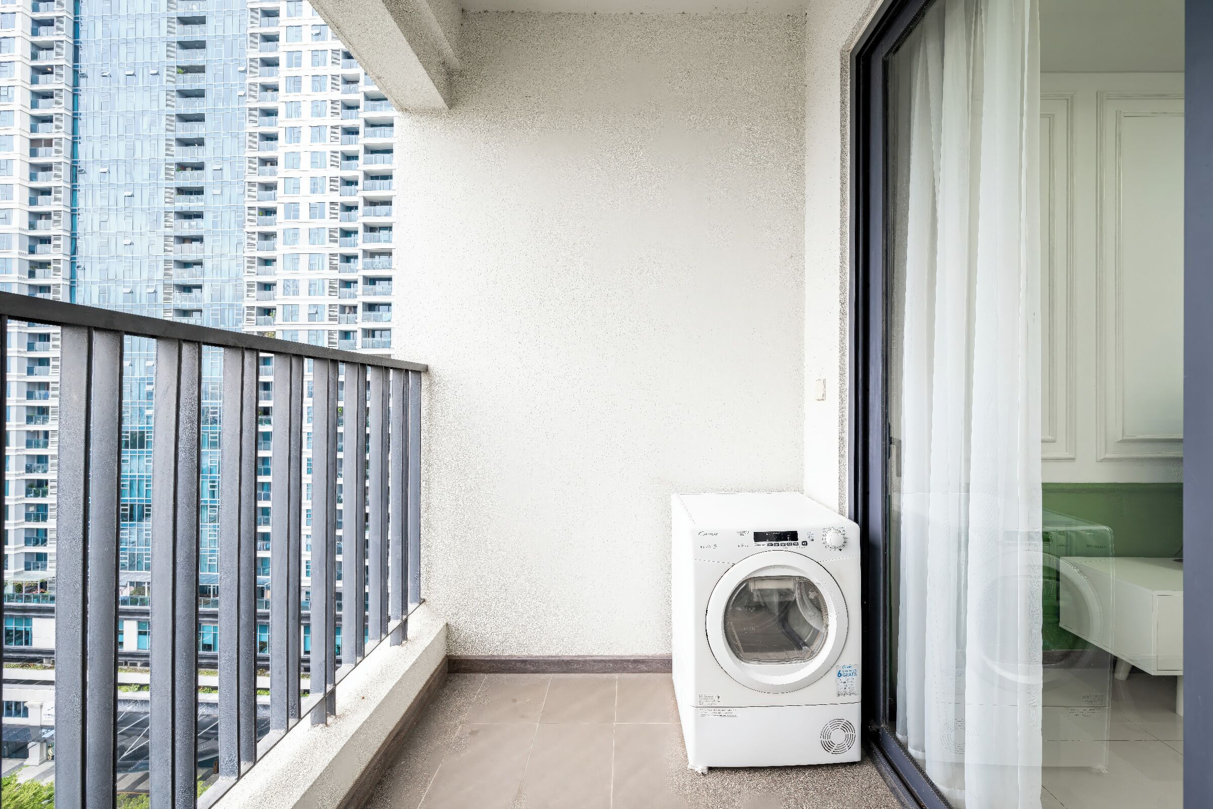 Un balcone con lavatrice, vista su edifici alti e una porta che dà su una stanza.