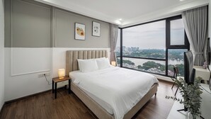 Une chambre moderne avec un grand lit, une table de chevet, un bureau et une vue sur le paysage urbain, visible à travers une grande fenêtre.
