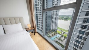 Une chambre d’hôtel dotée d’un grand lit, d’une table de chevet et offrant une vue sur le paysage urbain et l’eau grâce à de grandes fenêtres du sol au plafond.
