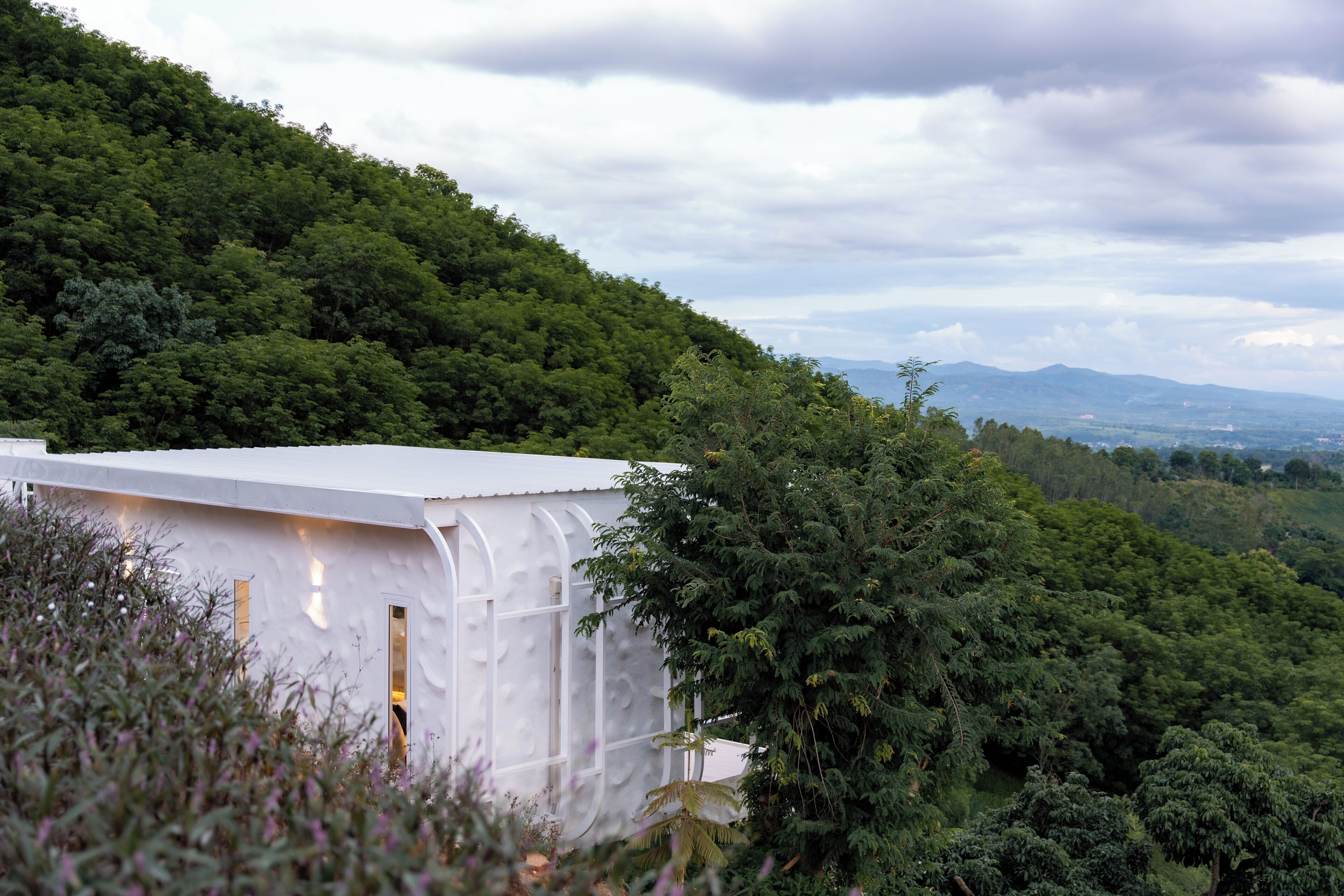 A white building with a curved roof nestled among lush green trees on a hillside.