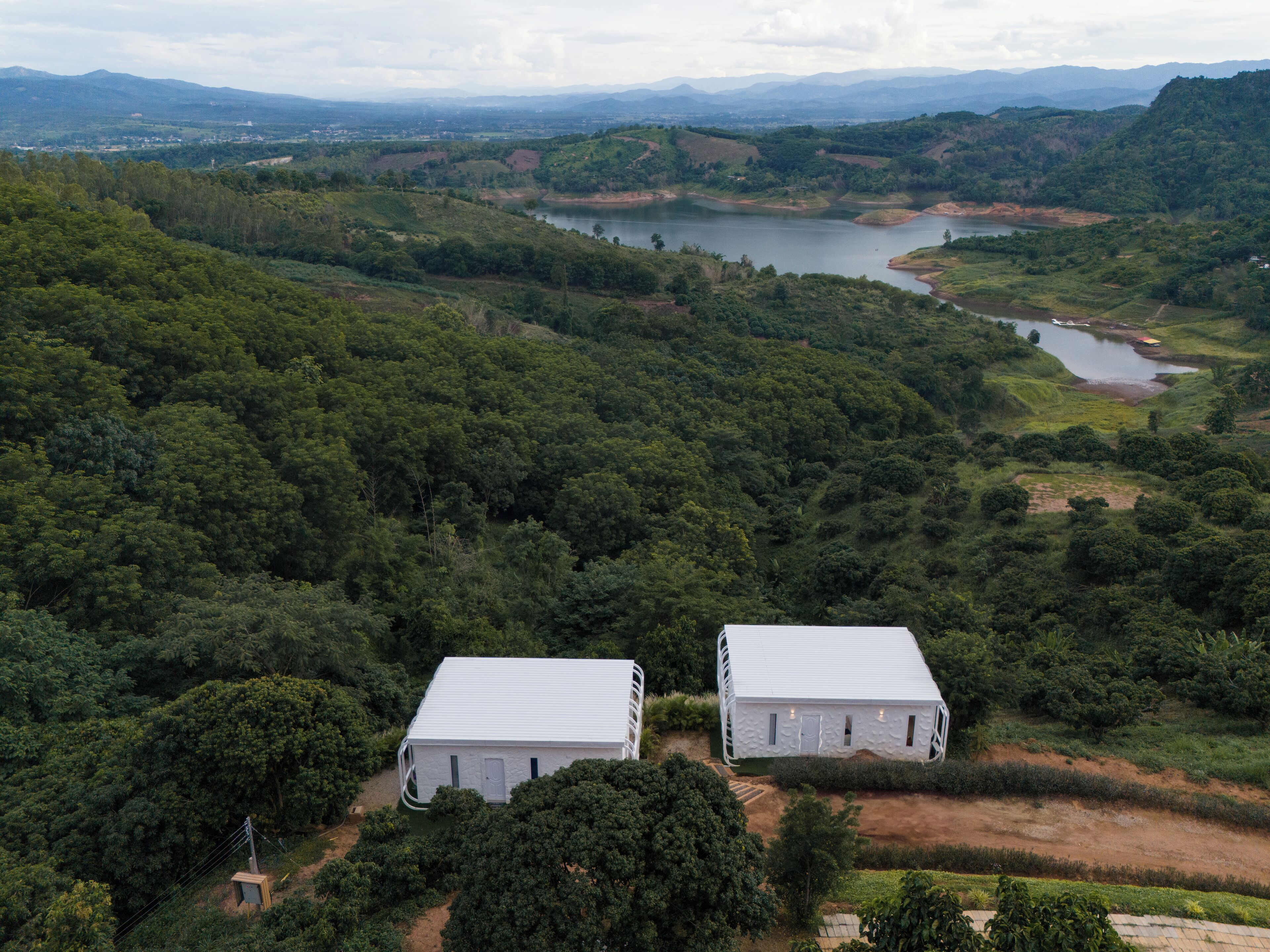 A remote, white, two-story building surrounded by dense forest and a lake.