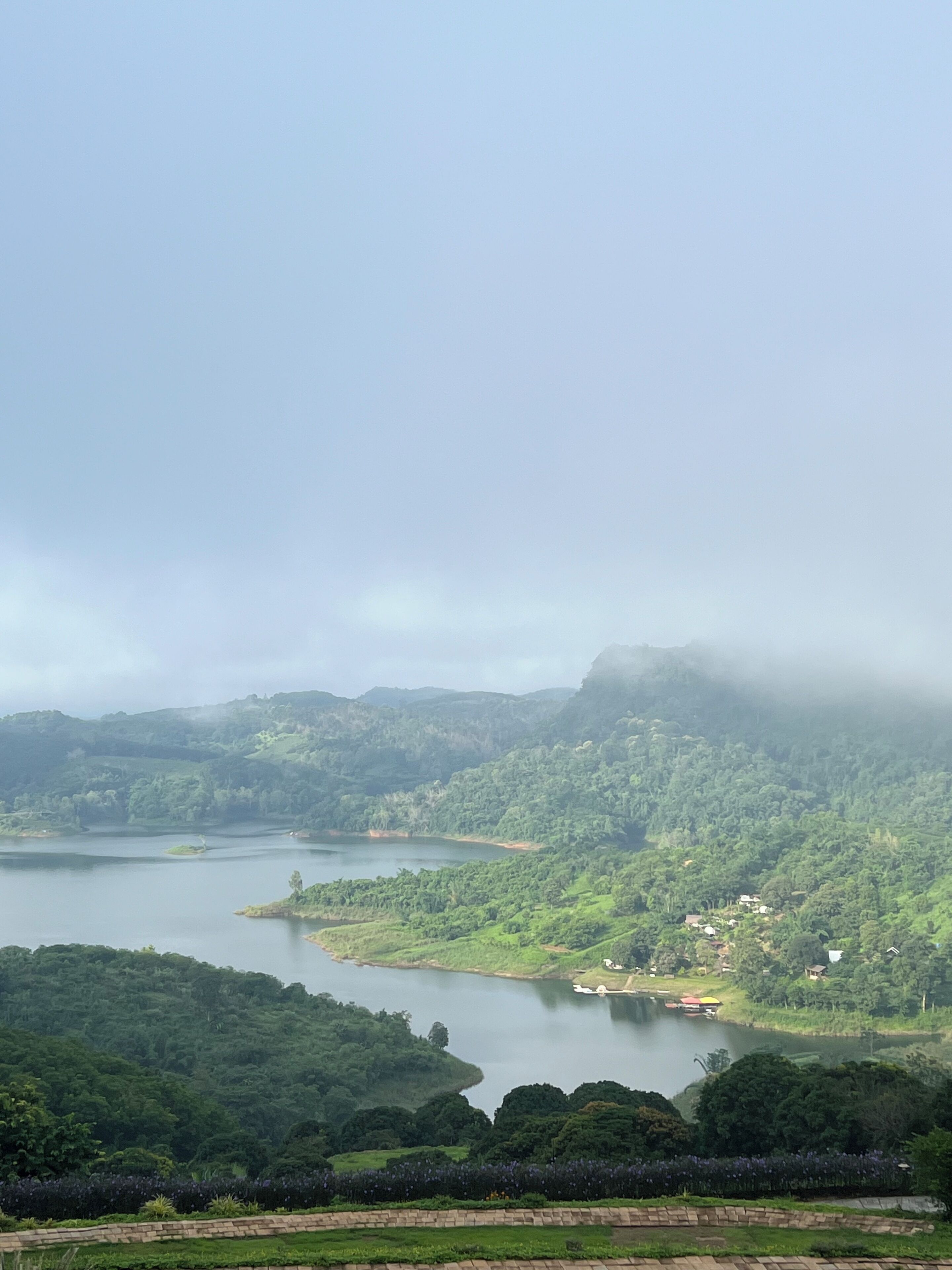Vista panorámica de un lago rodeado de colinas verdes exuberantes y algunos edificios dispersos.