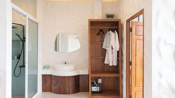Une salle de bain avec un lavabo blanc, un meuble-lavabo en bois et une étagère en bois où sont rangées des serviettes.