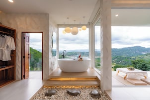 Une salle de bain moderne avec une baignoire sur pieds, une armoire en bois et une vue sur un paysage montagneux grâce à de grandes fenêtres.