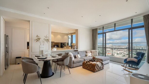 A modern living room with a large window, a sofa, a coffee table, and a dining area with chairs and a table. - City Garden Suites - Panorama Penthouse (Ho Chi Minh City)