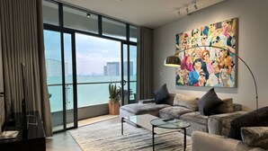 A modern living room with a large window, a sofa, a coffee table, and a painting on the wall. - City Garden Suites - Panorama Penthouse (Ho Chi Minh City)